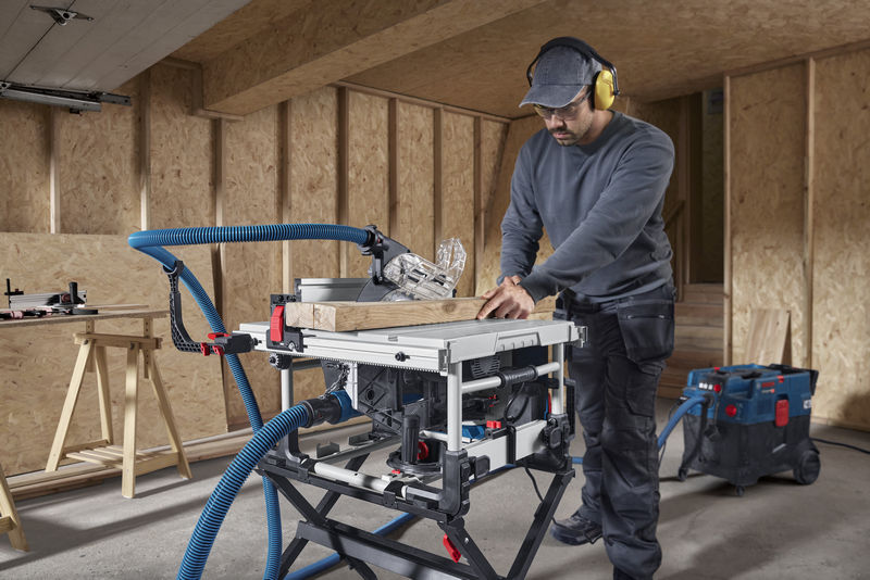 Eine Person mit Sicherheitsausrüstung führt in einer Werkstatt mit einer Tischkreissäge einen Holzschnitt durch. Anwendungsbild