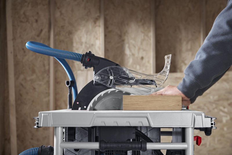 Eine Person führt in einer Werkstatt Holz durch eine Tischkreissäge. Anwendungsbild Nahaufnahme